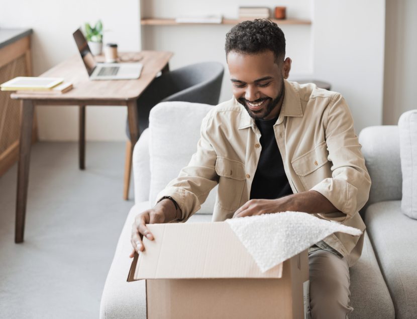 Happy man opening parcel at home, handsome guy opens package indoor, delivery, shipment, satisfied customers concept.